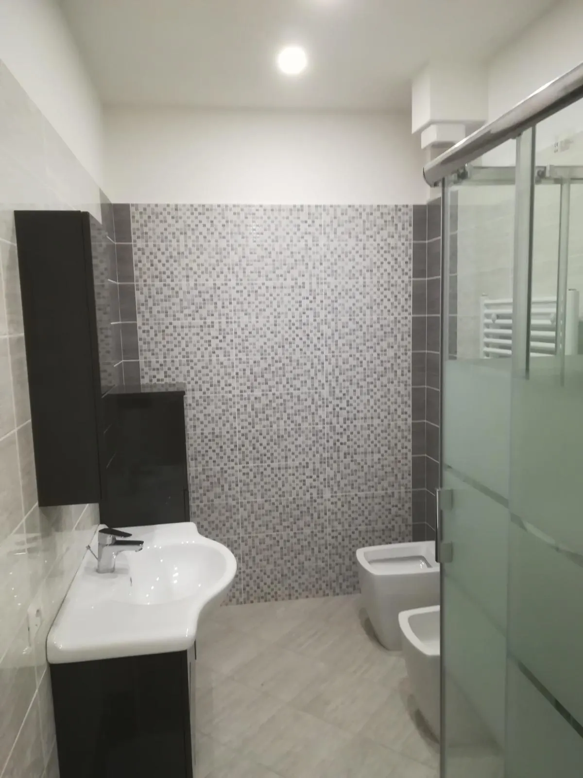 Bagno con rivestimento a mosaico e doccia in vetro